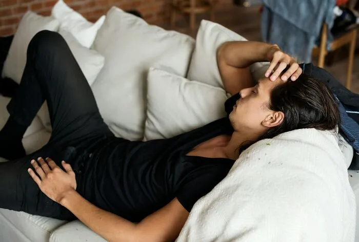 Young man lying on couch appearing tired and stressed, illustrating moments related to good or bad genes experiences.