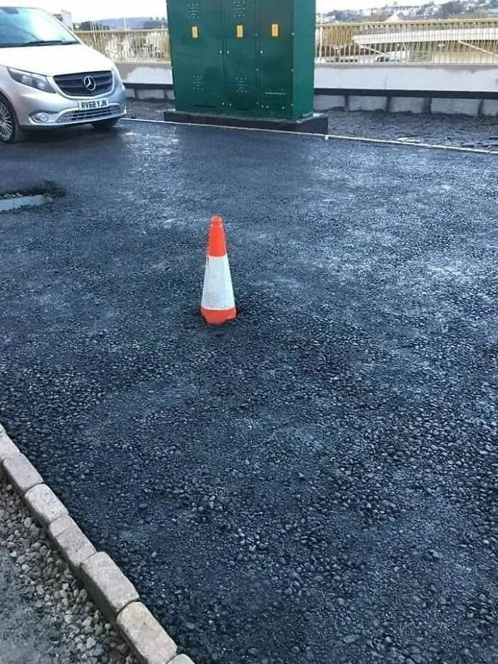 Traffic cone standing on freshly laid gravel, illustrating a weird pics or it didn’t happen moment in an outdoor parking area.