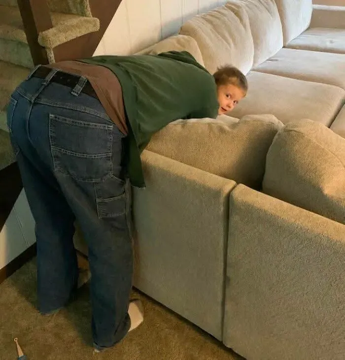 Child peeking over couch while an adult bends over nearby in a weird pics or it didn’t happen moment.