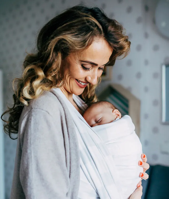 Mother smiling and holding her sleeping baby close in a cozy wrap, representing twins with unique and unusual names.