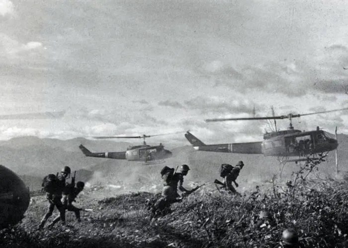 Black and white image of soldiers disembarking from helicopters during a historical military operation in a rugged landscape.