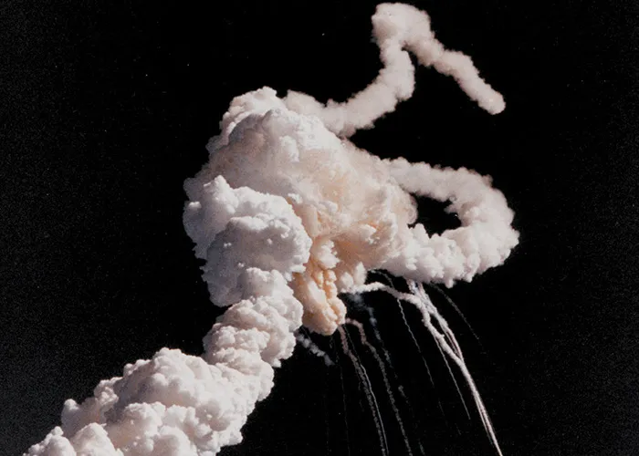 Smoke trail from a space shuttle explosion in a dark sky, depicting one of the most tragic historical events.