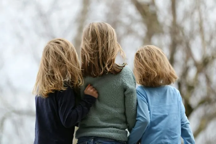 Three children with blonde hair stand outdoors with their backs facing the camera, highlighting unique names like Donwanna and Doneeda.