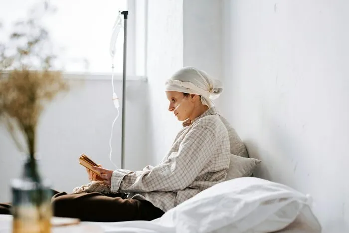 Young patient with IV drip, wearing a headscarf, resting in bed and reading, illustrating stories of good or bad genes.