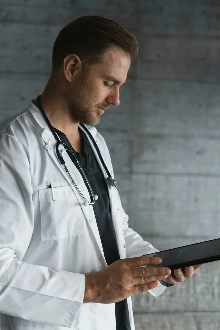 Young male doctor in white coat with stethoscope, reading digital tablet reflecting out-of-touch statements recalled by people