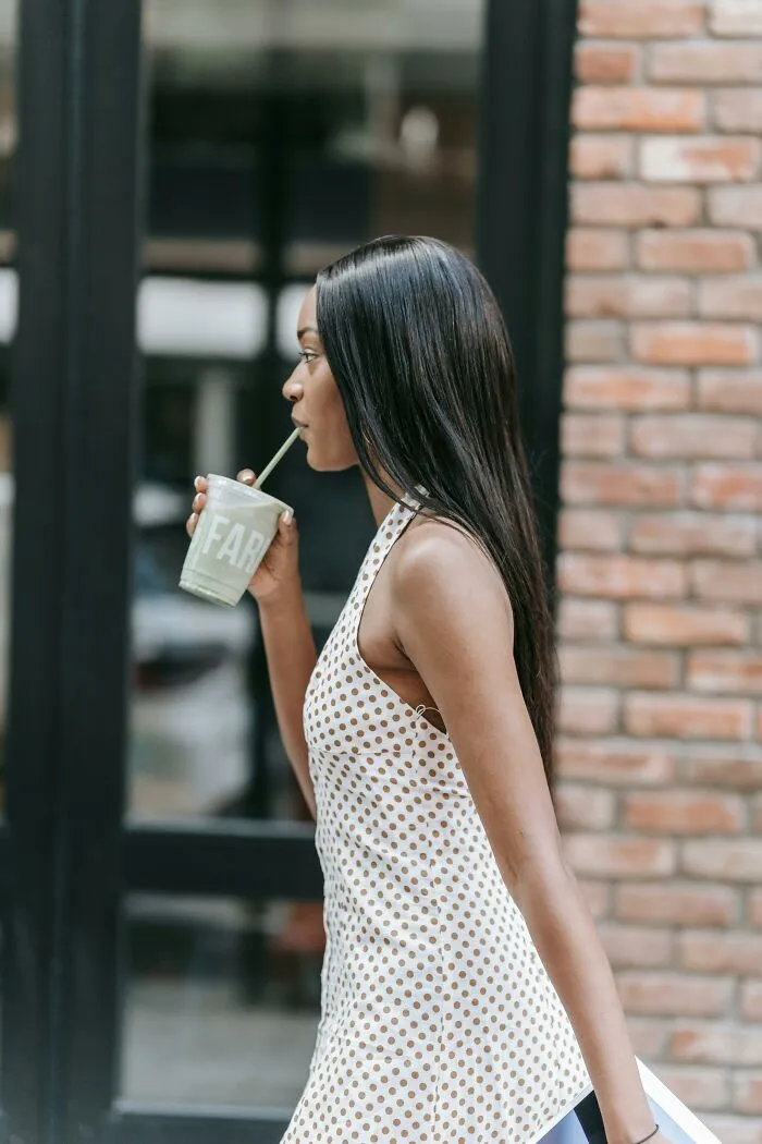 Young woman in polka dot dress drinking a green smoothie outside, reflecting on out-of-touch moments that make blood boil