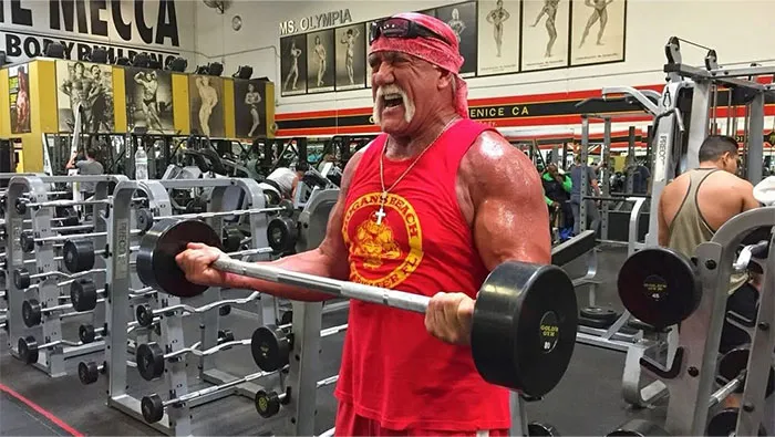 Hulk Hogan lifting dumbbells at a gym, showcasing strength and intensity related to Steve Jobs celebrity contrasts.