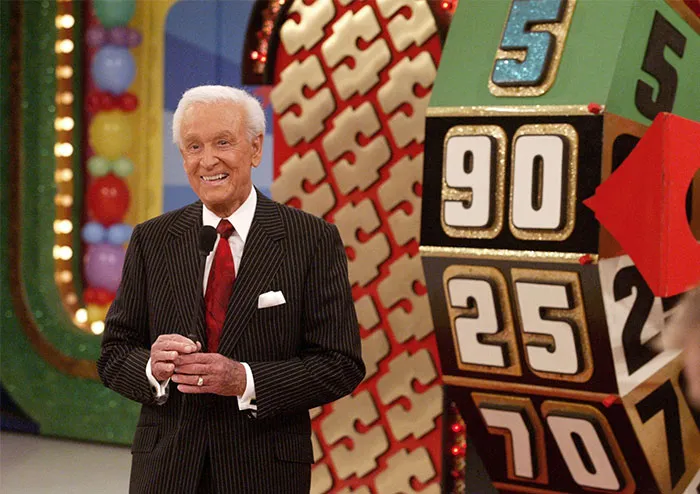 Game show host standing near a spinning wheel on a colorful set, related to Steve Jobs celebrity comparisons.