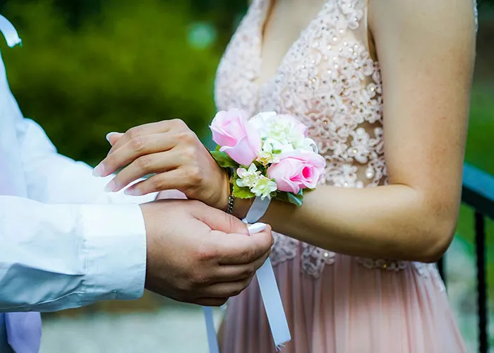 Man placing a pink rose corsage on a woman’s wrist, illustrating themes of cheating partners and betrayal in relationships.