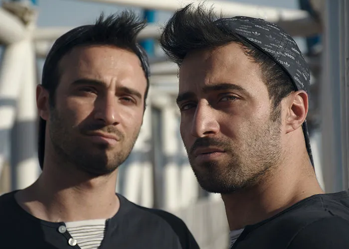 Two men with serious expressions outdoors in casual clothing, illustrating themes of cheating partners and exposure.