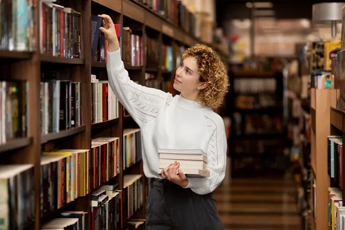 Young woman in a library selecting books, representing things folks only romanticize without truly experiencing them.