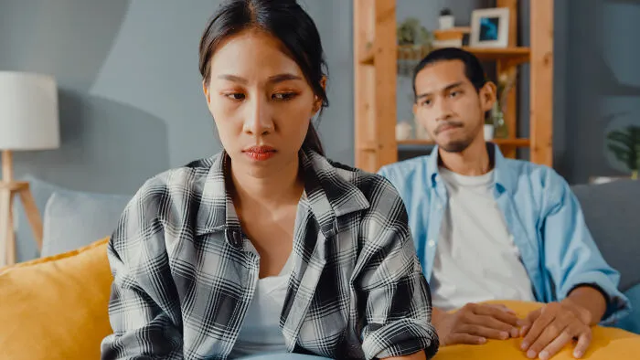 Couple having a serious conversation on sofa, highlighting the concept of romanticizing experiences without truly living them.