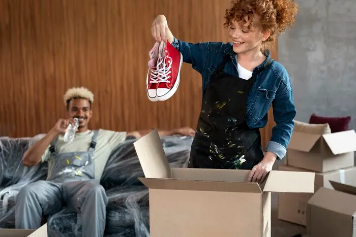 Young couple experiencing moving day, unpacking boxes and holding sneakers, showing moments people only romanticize.