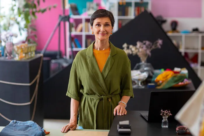 Middle-aged woman in green robe standing in a cozy room, symbolizing things folks only romanticize without experience.