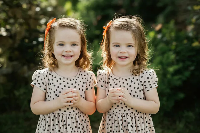 Two young girls with curly hair and polka dot dresses smiling outdoors, illustrating things folks romanticize.