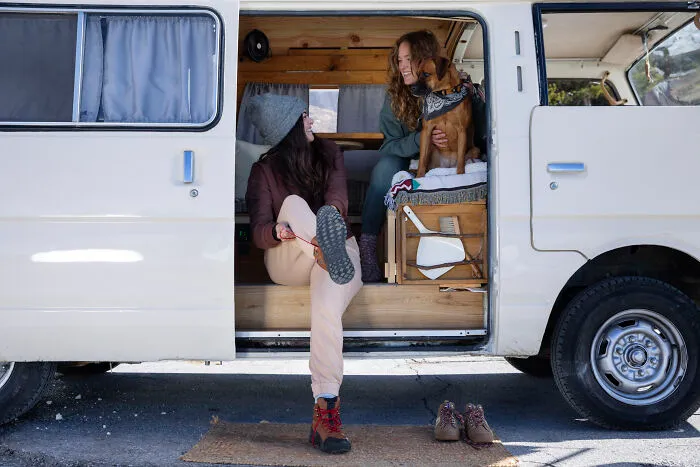 Two women enjoying a van life road trip with a dog, capturing the essence of romanticized adventurous experiences.