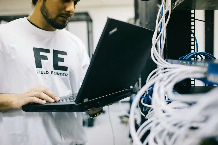 Tech guy working on a laptop surrounded by network cables, discovering something weird or disturbing during computer repair.