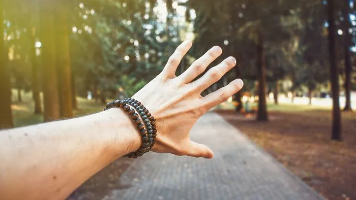 Hand wearing cringey nineties fashion beaded bracelets reaching out on a sunlit forest path in autumn.
