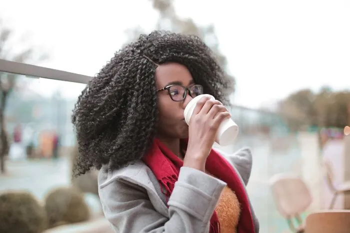 Woman with curly hair and glasses drinking coffee outside, illustrating changes in restaurant food purchases.