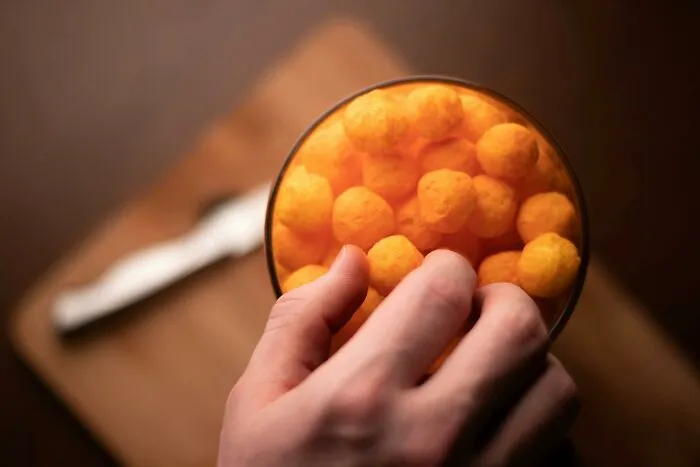 Hand reaching into a bowl of cheese puffs, illustrating side-by-side comparisons of food prices in the 1980s and now.