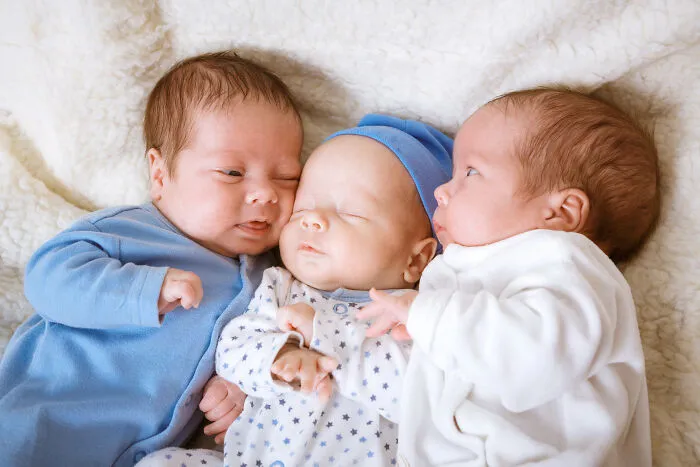 Three newborn twins lying close together on a soft blanket, showcasing unique and playful baby names.