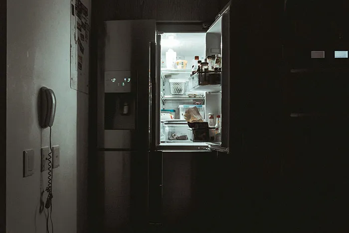 Refrigerador abierto en cocina oscura simbolizando momentos de parejas que se han dado cuenta de que su pareja es idiota.