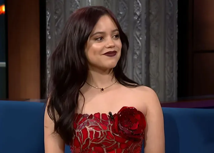 Young woman in a red floral dress smiling during a television interview about people who knew celebrities before fame.