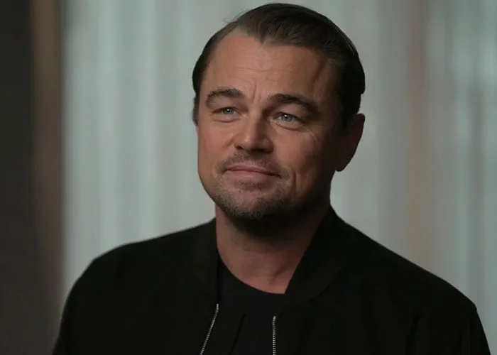 Man with slicked-back hair and black jacket smiling softly in an interview about people who knew celebrities before fame reveals