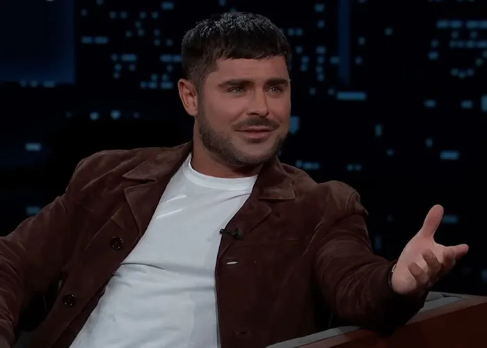 Actor wearing a brown jacket and white shirt sharing stories with people who knew celebrities before fame on a talk show.