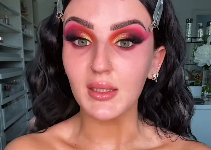 Young woman with dramatic colorful eye makeup revealing celebrity personality before fame in casual indoor setting.