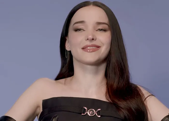 Young woman with long dark hair smiling confidently against a solid background, sharing stories from people who knew celebrities before fame.