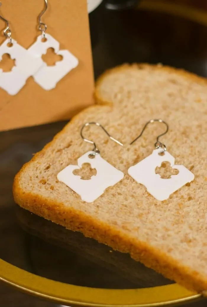 Earrings made from white plastic bread bag clips displayed on a slice of bread in a DIY craft shaming project.