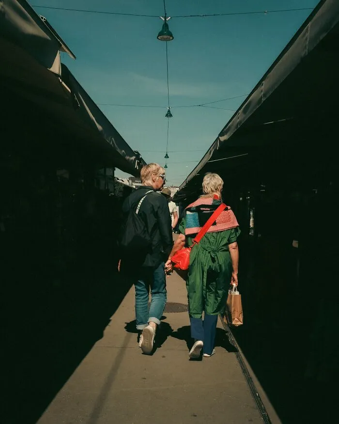 Urban street photo by Helsinki-based photographer showing two people walking between market stalls in natural light.