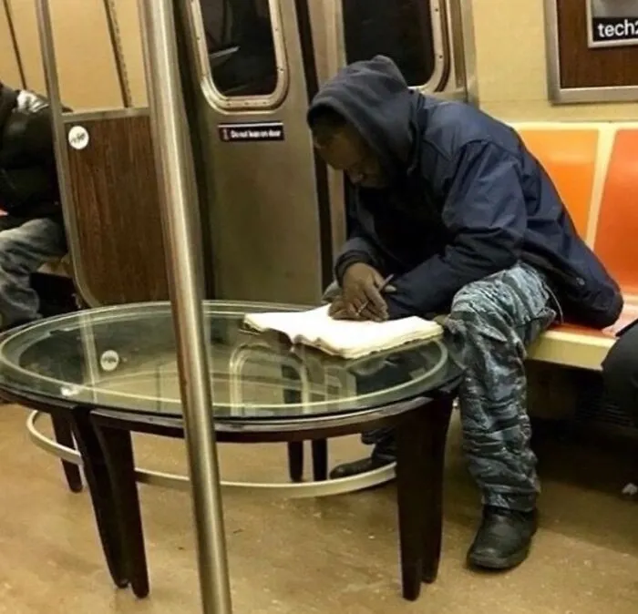 Man writing in a notebook on a subway with a glass table in front, an image that might make you uncomfortable.
