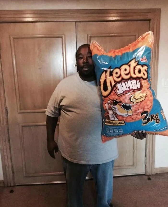 Man holding an oversized jumbo bag of Cheetos snacks indoors, an image that might make you uncomfortable.