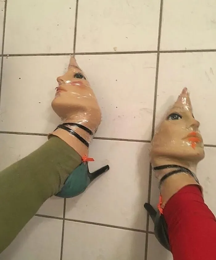 High-heeled shoes designed with realistic human faces, creating a visually uncomfortable image.
