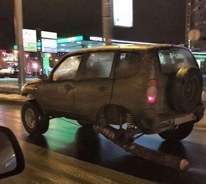 Car driving at night with large log replacing rear wheels, an uncomfortable and strange roadside scene.