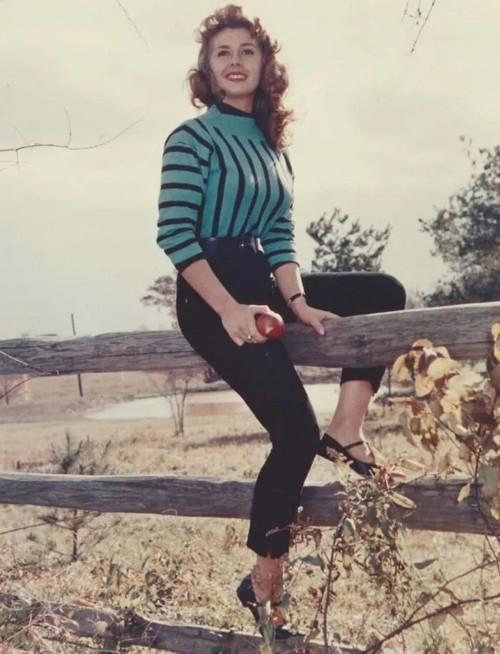 Young woman in vintage clothing sitting on a wooden fence holding an apple in a rural setting vintage photos history