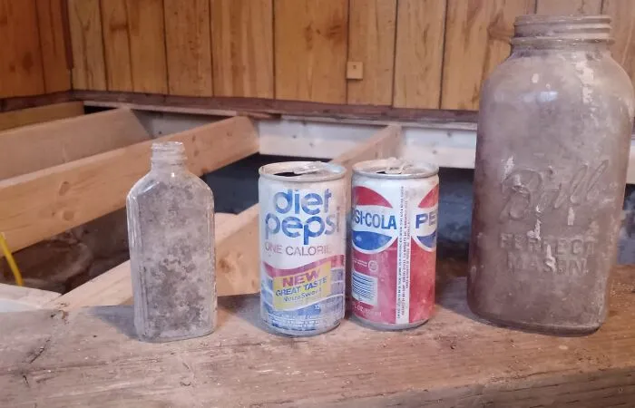 Old dusty bottles and soda cans found in walls and hidden places inside a home under renovation.
