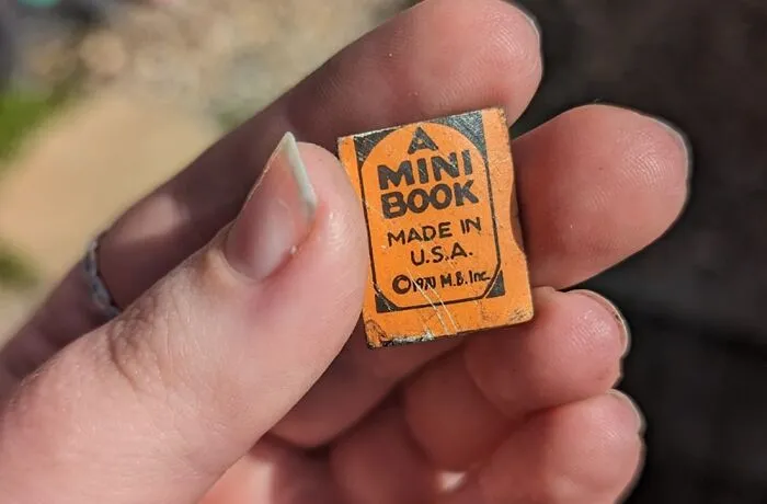 Close-up of a hand holding a tiny vintage mini book, an unexpected thing found in walls and hidden places in homes.