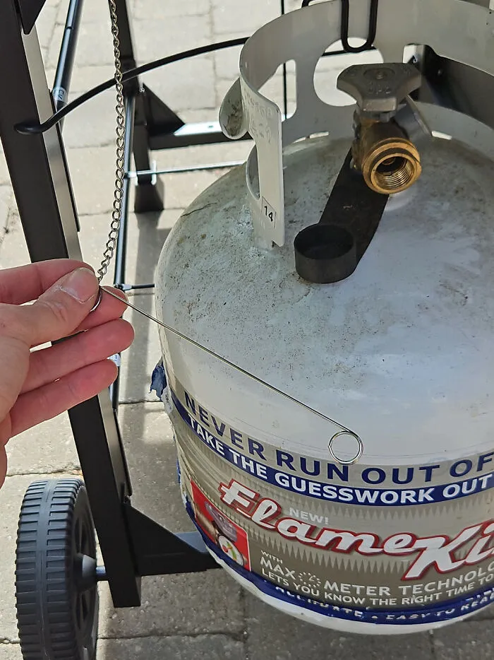 Hand holding a metal chain hook near a propane tank valve, a mystery object recognized by an online group.