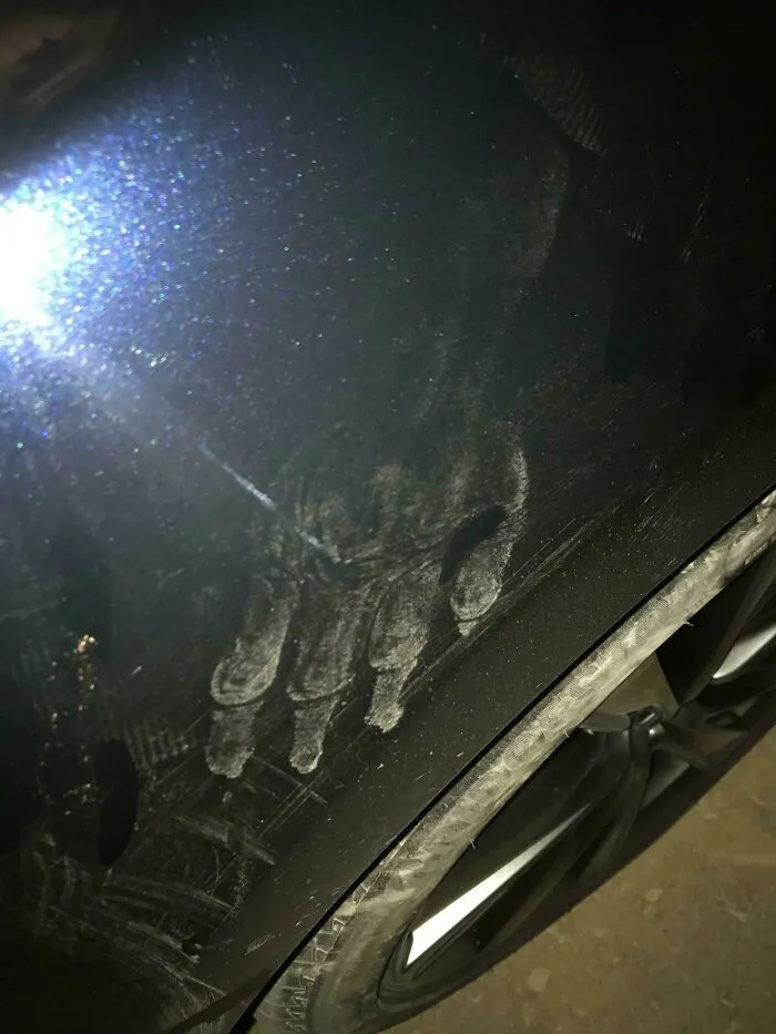 Disturbing photo of a dirty handprint on a car door near the wheel, captured in low light with a bright glare.