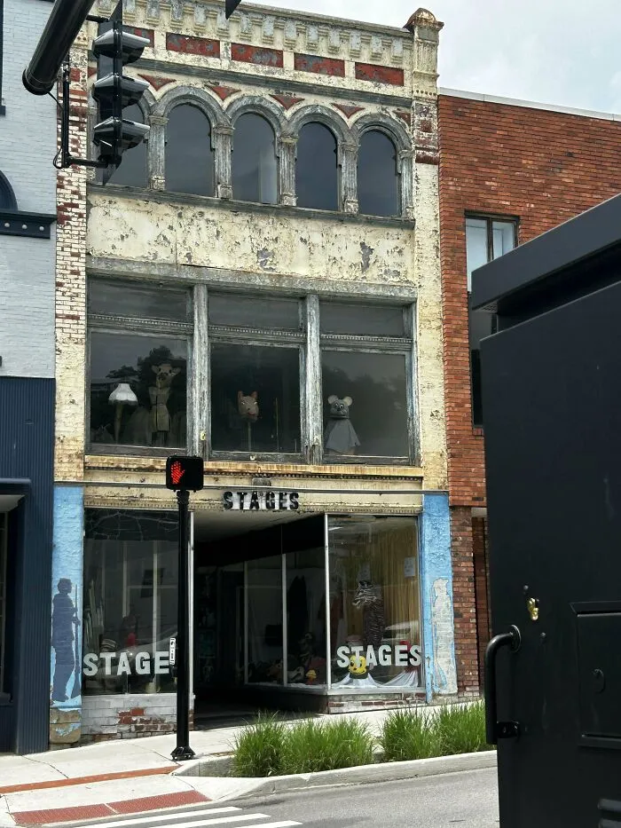 Disturbing old building facade with dark windows displaying unsettling mannequins, evoking eerie and creepy vibes.