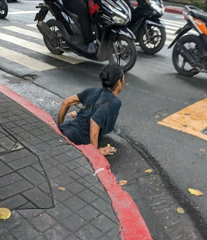 Person trapped in a street sinkhole near traffic, a disturbing photo likely to make you sleep with the lights on.