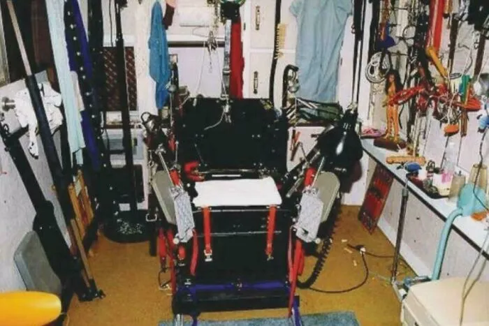 Old electric chair surrounded by various tools and equipment in a dimly lit room, a disturbing photo scene.