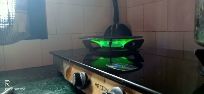 Green gas stove burner lit with a pan on top, a funny pic capturing an utterly confused moment in cooking.