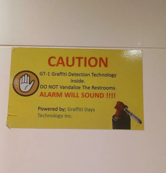 Caution sign warning of graffiti detection technology and alarm in restrooms, shown in a funny and confusing context.