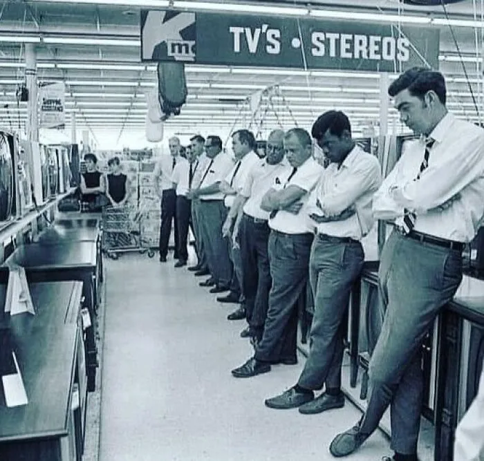 Men lined up in a store aisle looking at TVs, illustrating weird things about history in a vintage setting.
