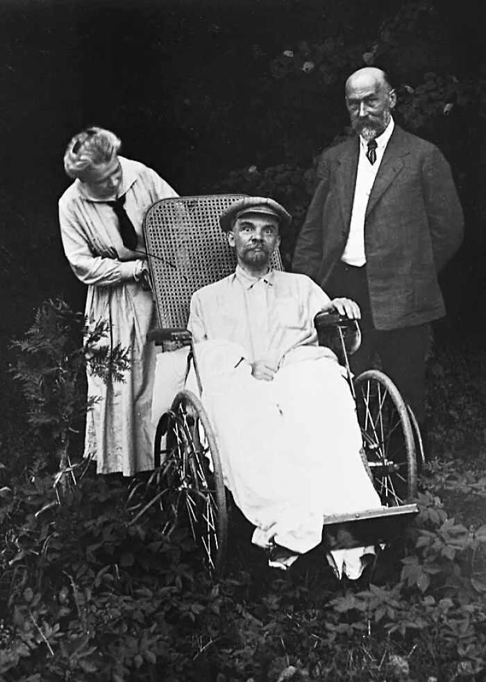 Black and white photo showing an elderly man in a wheelchair with two people standing beside him, last known photos famous people.
