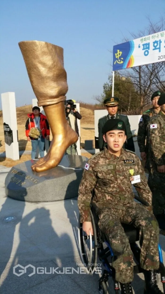 South Korean soldier in wheelchair beside large bronze leg sculpture symbolizing traumatizing the next generation.